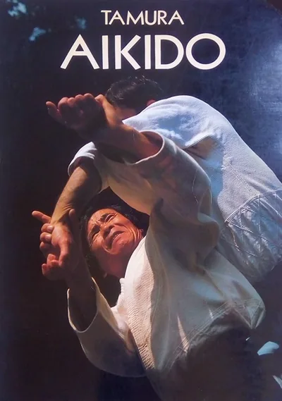 Cover of Aïkido (1986): “TAMURA” and “AIKIDO” in white capitals above a color photo of a throw, two aikidoka in white keikogi against a dark background